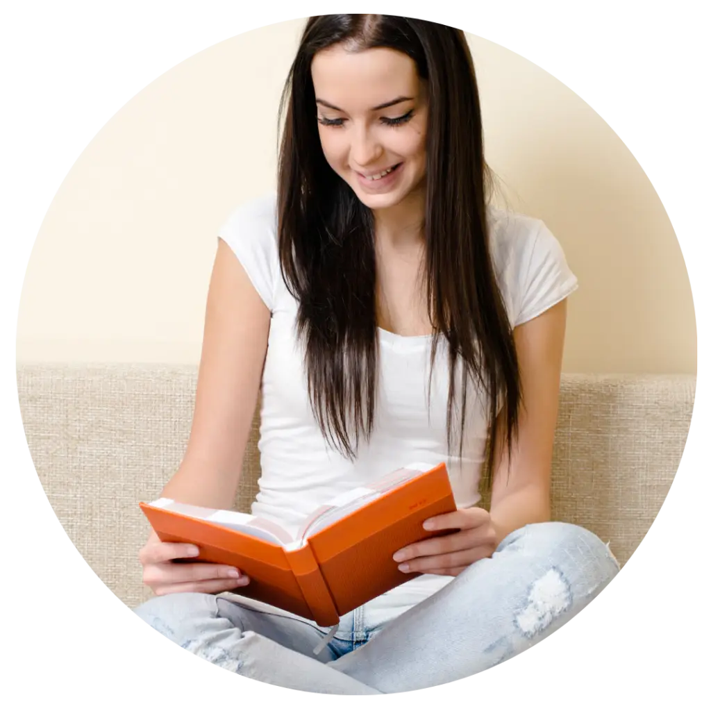 Teen girl reading an orange book on beige couch, smiling