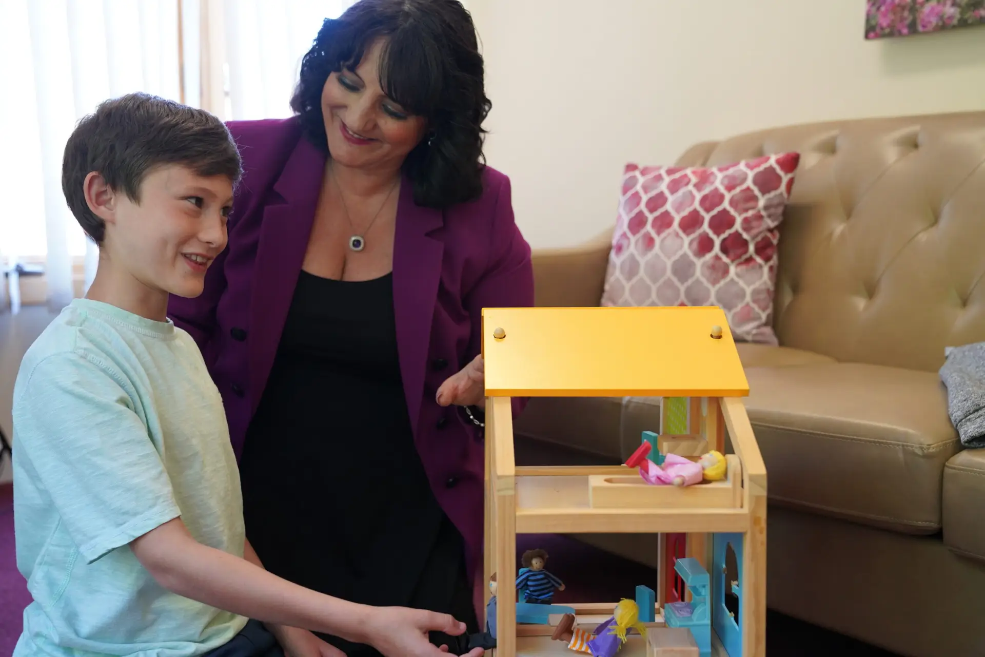 Child and therapist engaging with a wooden toy house during a play-based learning session