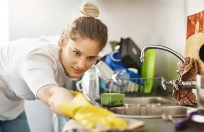Woman in white shirt wearing yellow gloves washing dishes