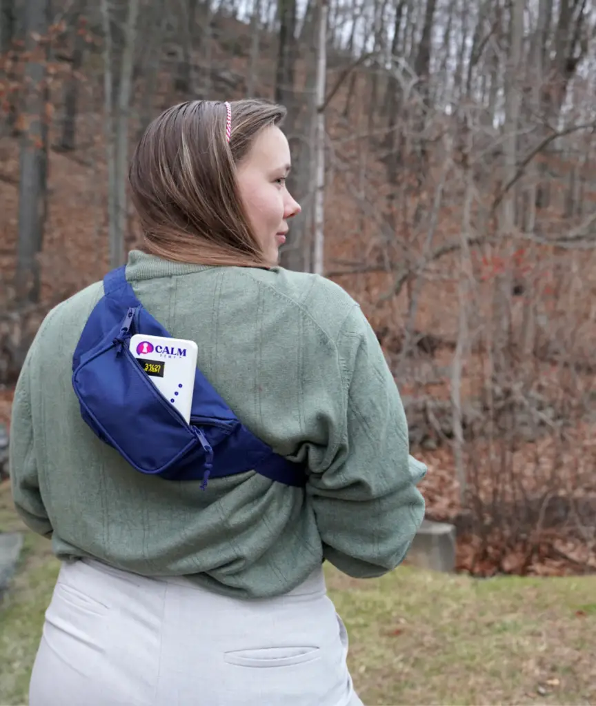 Teenage girl from behind wearing blue CALM fanny pack over cardigan, outdoors