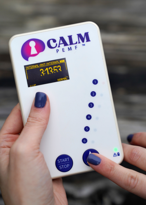 Hands holding white CALM PEMF device with digital display