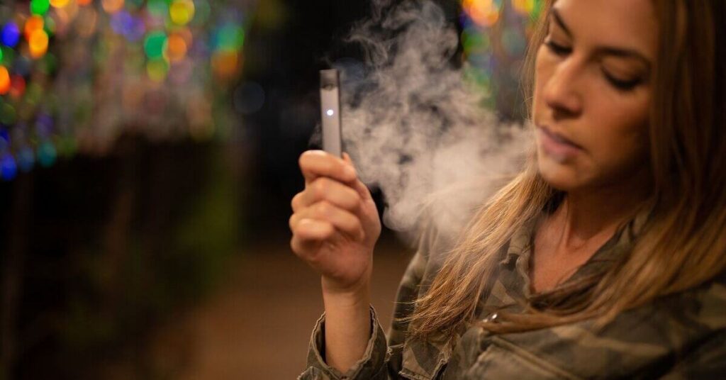 A woman vapes in front of lights.