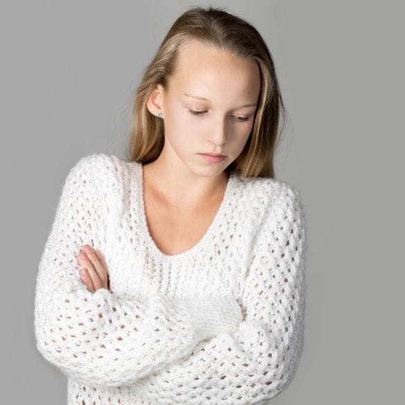 A traumatized young girl experiencing PTSD, dressed in a white sweater, tightly folding her arms.
