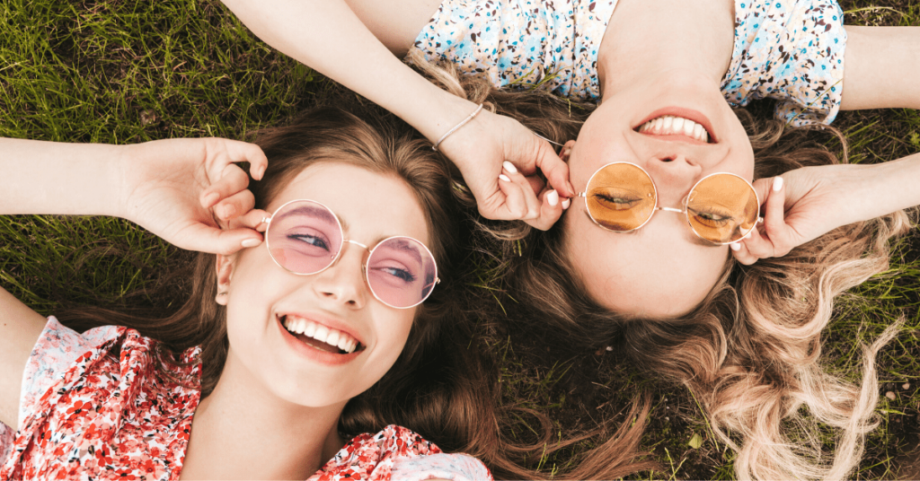 Two young women enjoying the sunny grass while wearing sunglasses, making 2020 their happiest year yet.