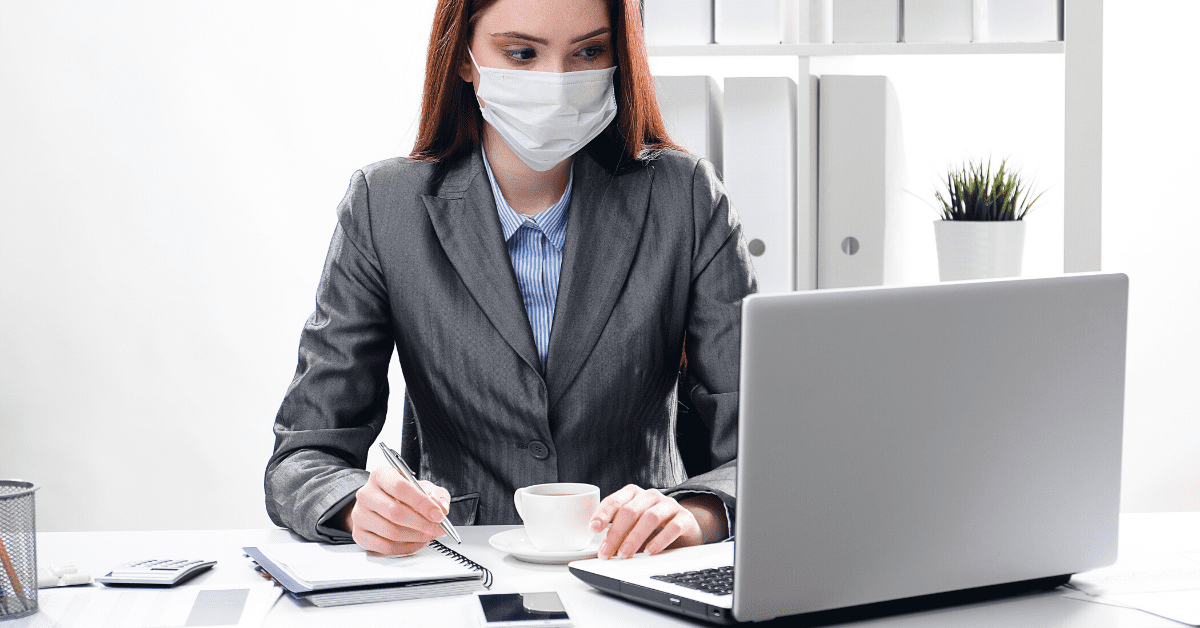 A woman practicing workplace safety by wearing a surgical mask at her desk.