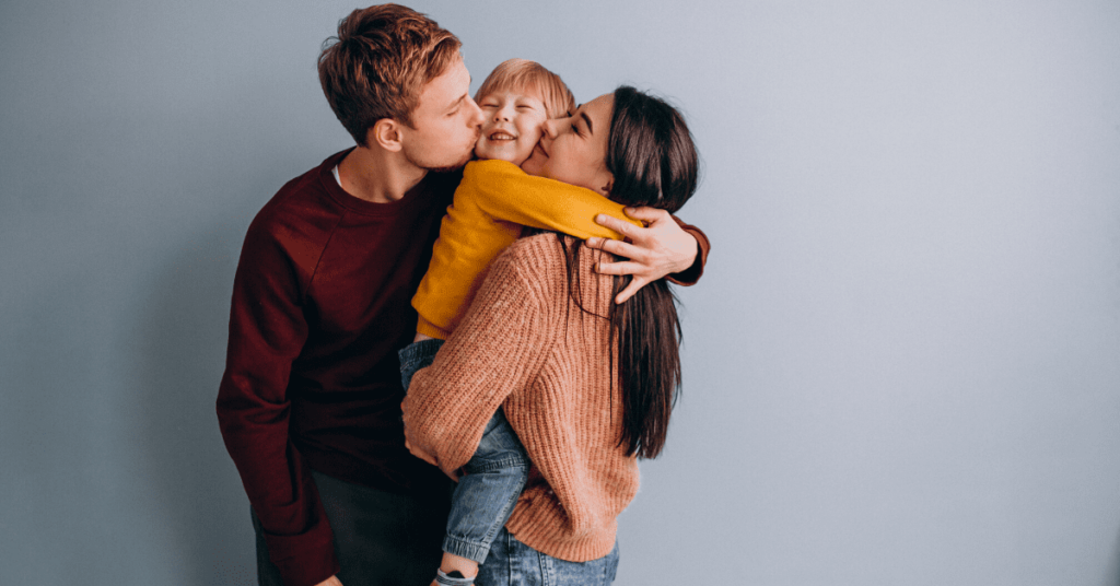 A family is embracing and affectionately kissing their child on a blue background, displaying the best parenting advice through love.