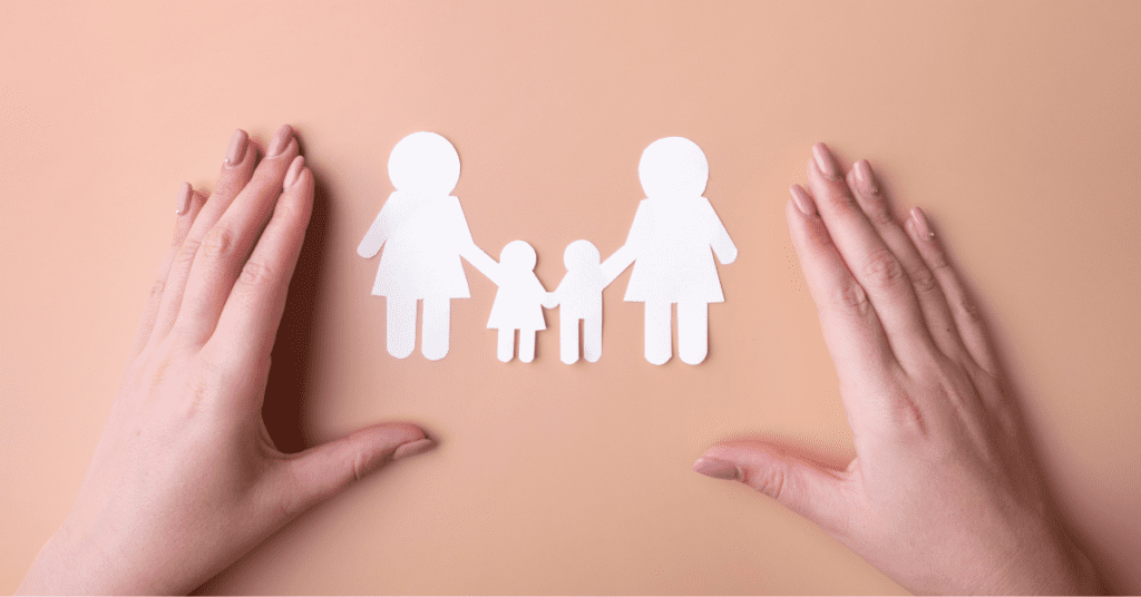 A woman's hands holding a paper cutout of a family on a background, representing same-sex parents.
