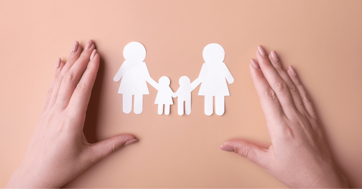 A woman's hands holding a paper cutout of a family on a background, representing same-sex parents.