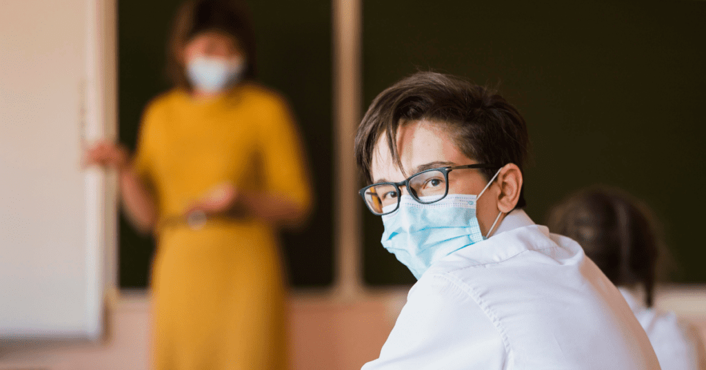 A student wearing a surgical mask receives guidance from a school psychologist on coping with the 'new normal' in a classroom setting.