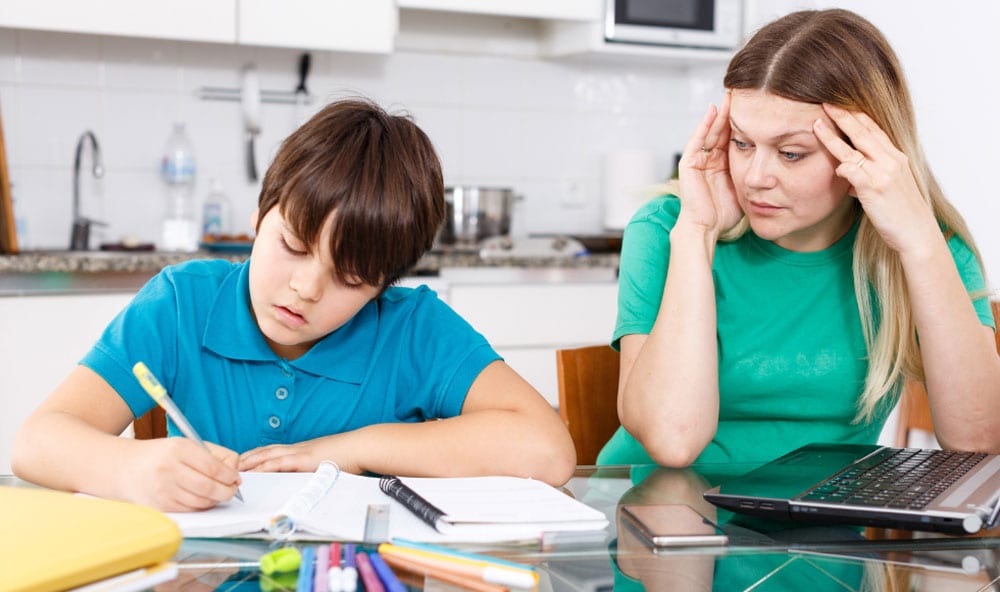 A mother and son working on homework in the kitchen.