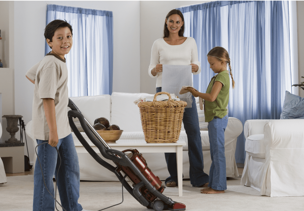 A woman engages kids in chores by holding a vacuum cleaner.