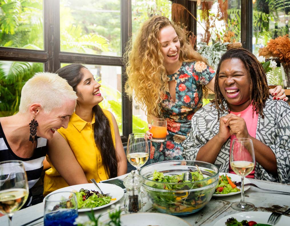 A group of friends laughing at a dinner table while discussing how fasting helps anxiety and depression.