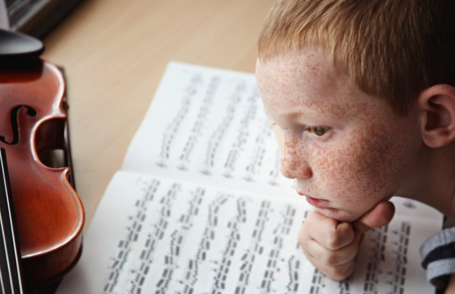 A young boy exploring a violin and music sheet in a media kit.