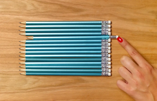 A person showcasing a blue pencil from a media kit on a wooden table.