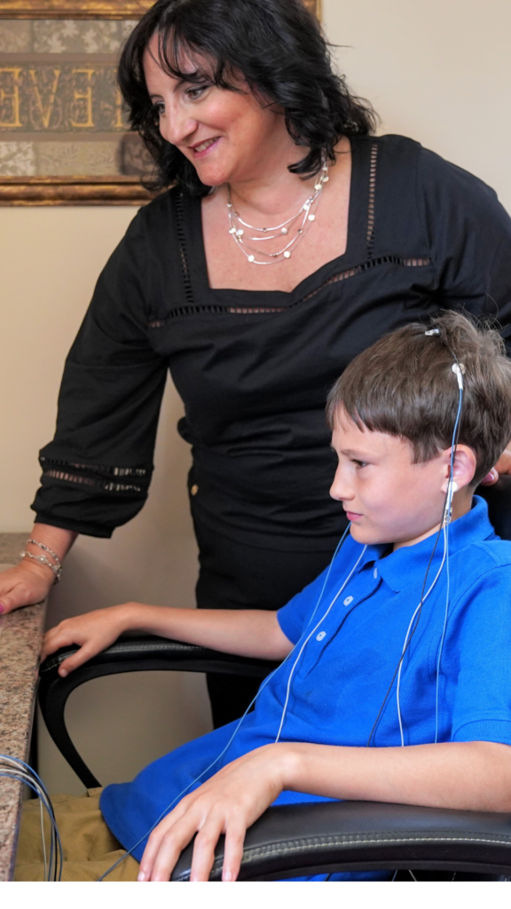 A woman is assisting a boy with his hearing aids, demonstrating how we can help.