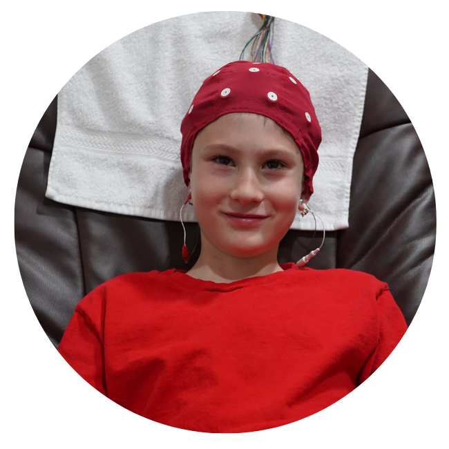 A young boy using neurofeedback technology, wearing a red polka dot hat.