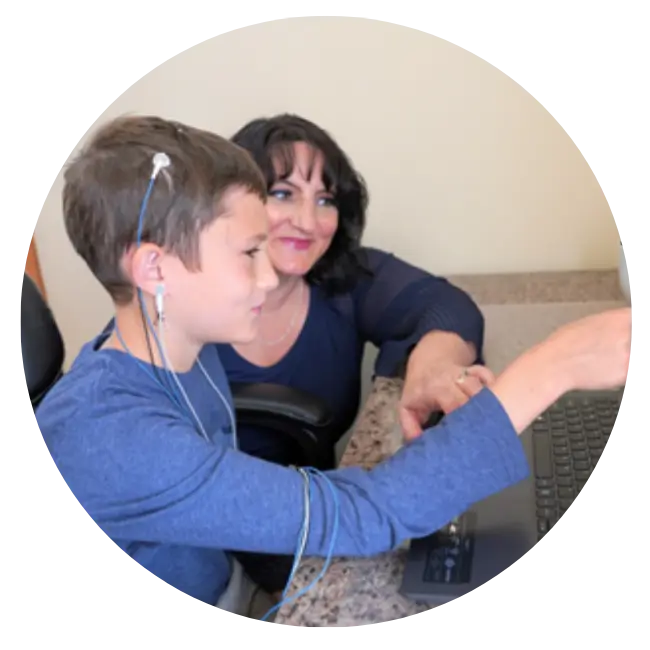 A woman and a boy utilizing neurofeedback while using a computer to explore their journey.